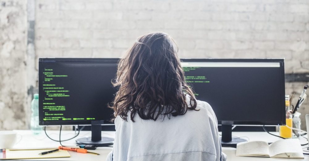 Rear view of female computer hacker coding at desk in creative office