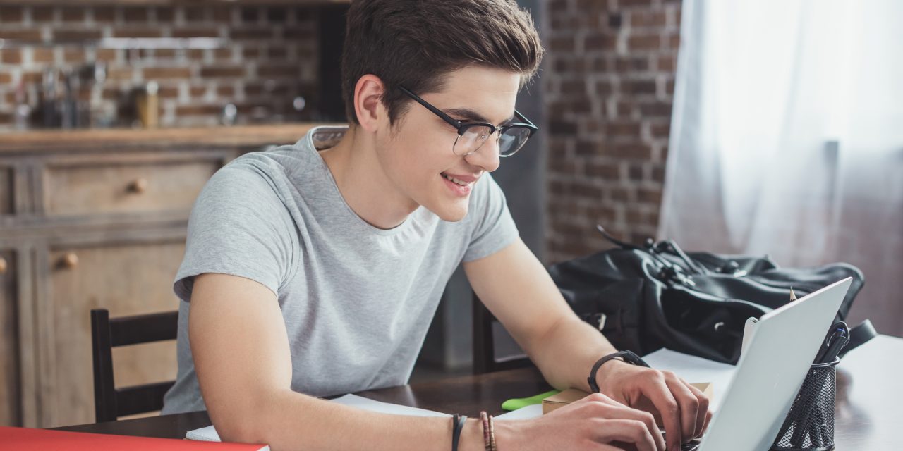 smiling student doing homework and typing on laptop